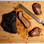 Juicy sliced brisket on a wooden cutting board with a sharp kitchen knife.